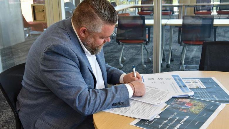 Man in a suit at a table writing on documents.